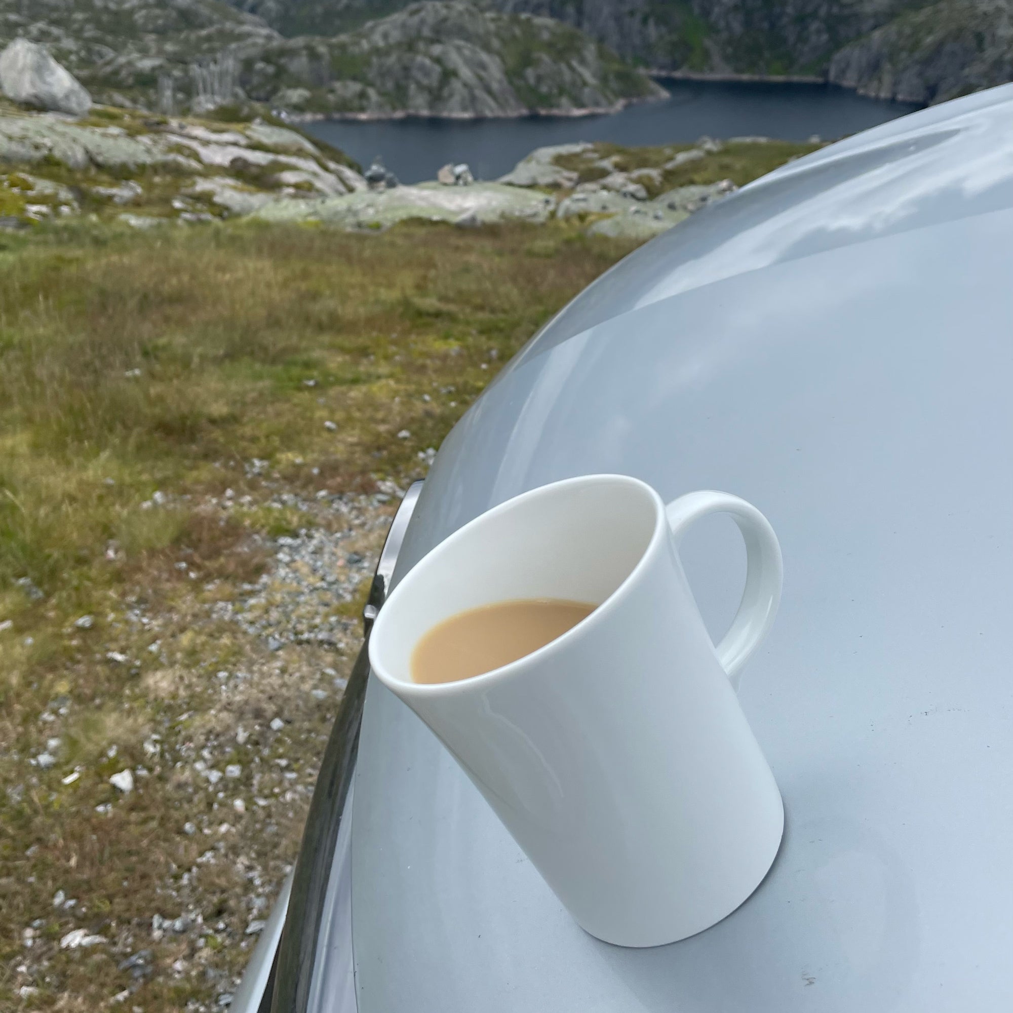 Magnet-Porzellan-Henkeltasse auf Motorhaube vor einem Fyord  