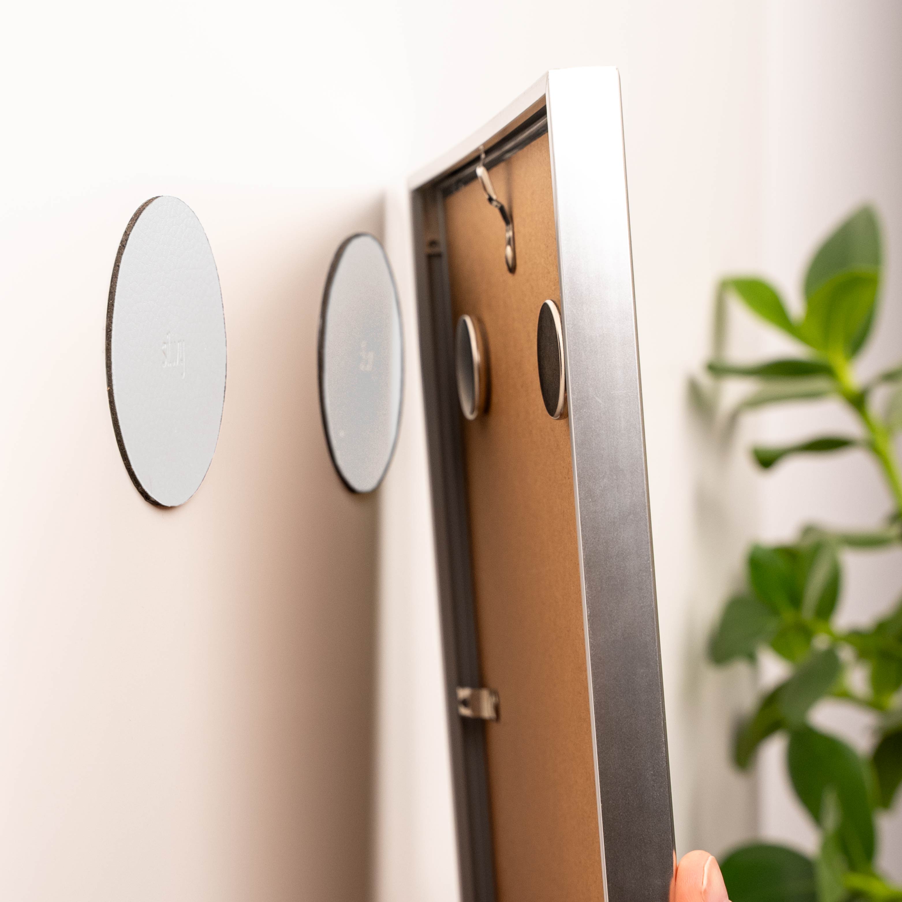 zwei runde Powermagnete an einem Bilderrahmen befestigt sowie zwei runde Metall-Nano-Gel-Pads in weiß an der Wand 