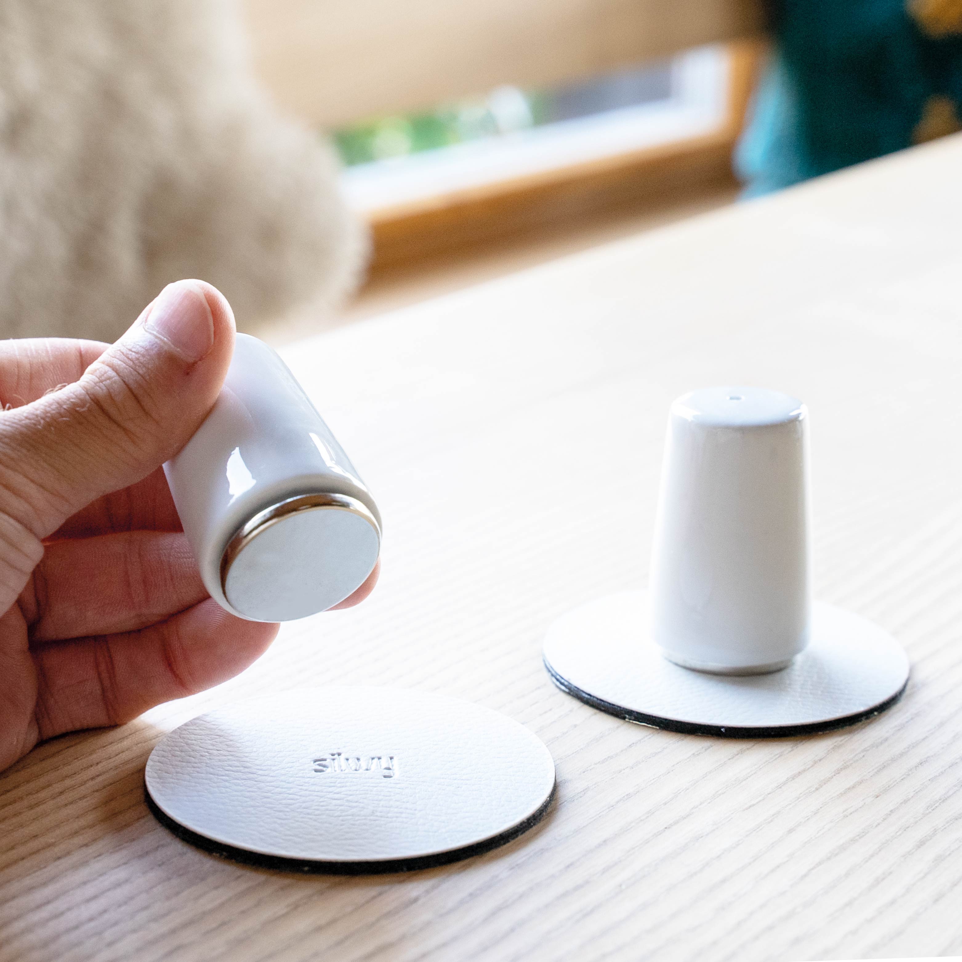 Zwei runde Power Magnete befestigt an Salz und Pfefferstreuer auf zwei weißen Metall-Nano-Gel-Pads 